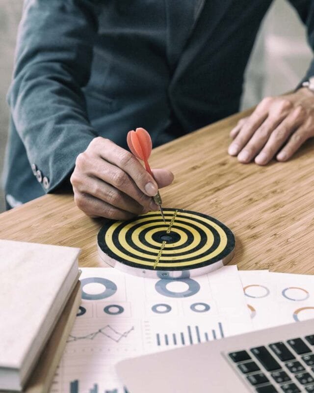 Asia Target Operating Model Strategies - A business professional aims a dart at a target on a desk, surrounded by charts and a laptop, symbolizing goal setting and focus.