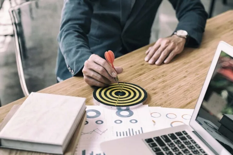 Asia Target Operating Model Strategies - A business professional aims a dart at a target on a desk, surrounded by charts and a laptop, symbolizing goal setting and focus.